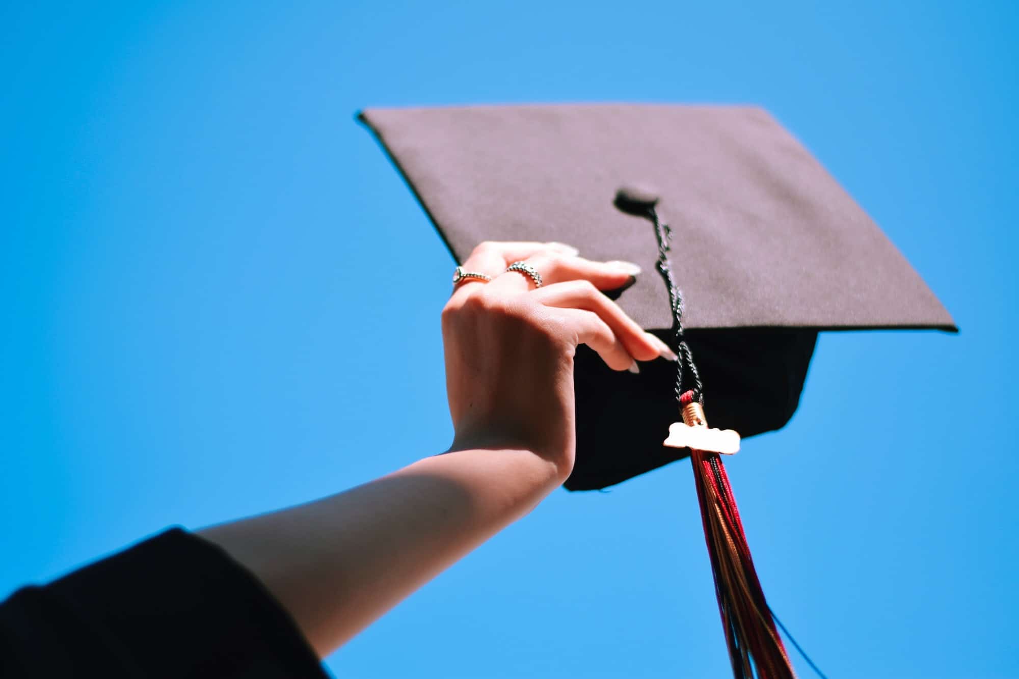 Girl is holding graduation cap up in the air against blue sky